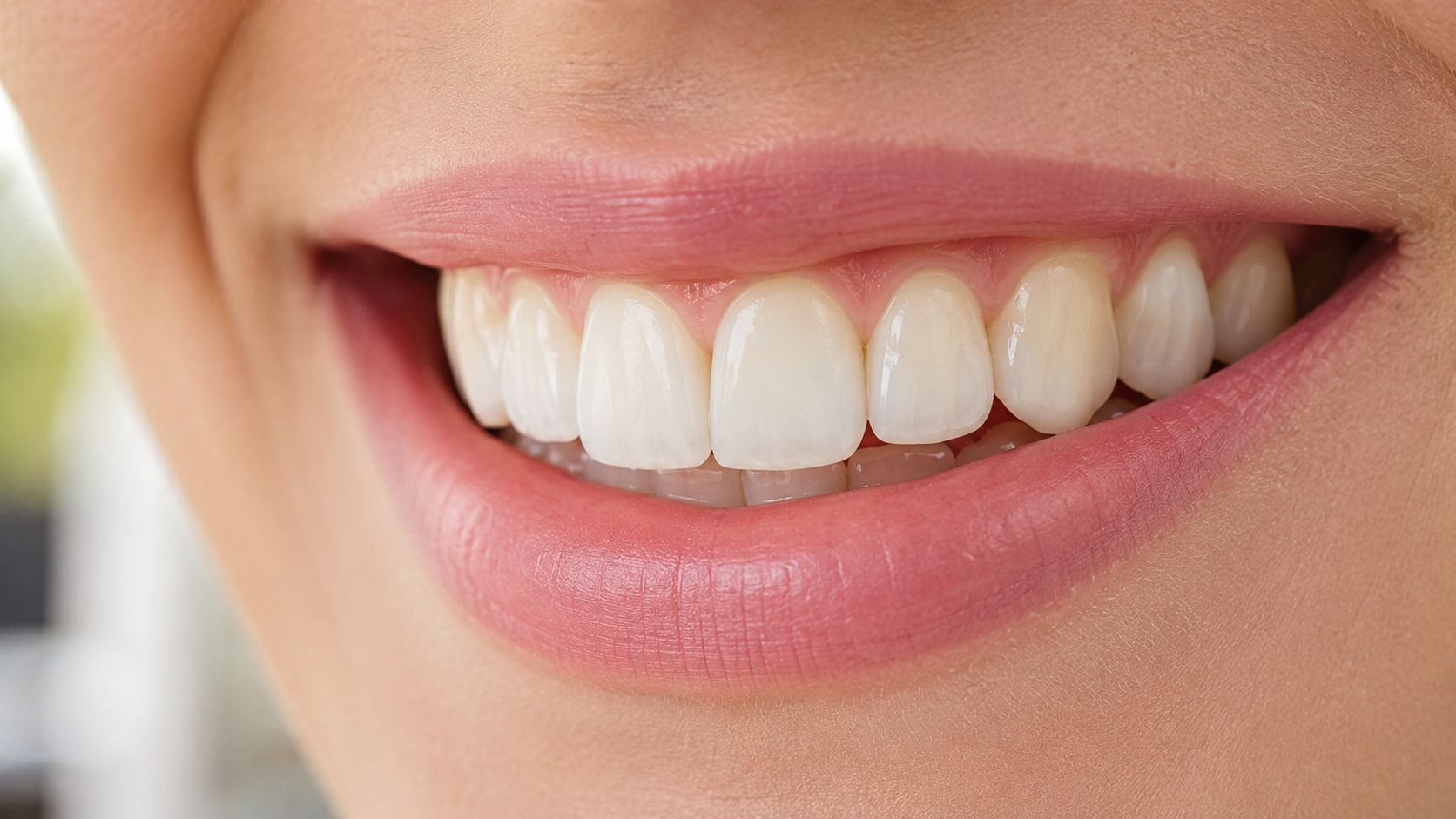 A close-up view of a woman's bright, healthy smile showcasing clean white teeth and pink lips.