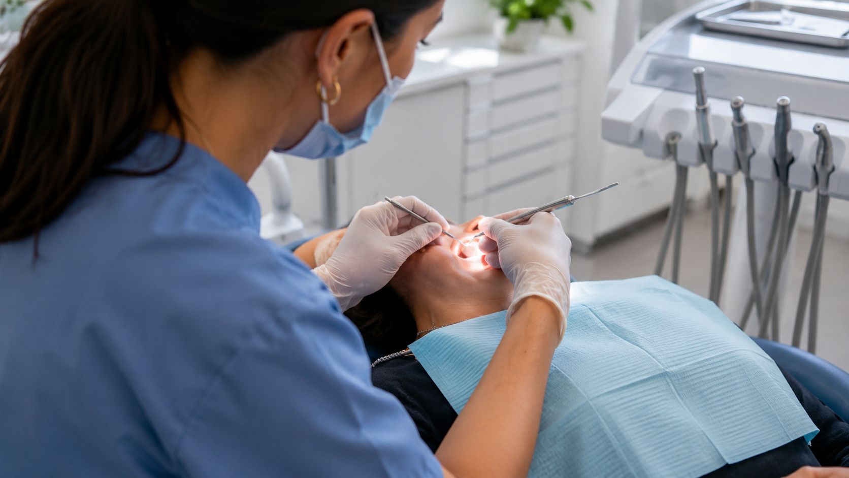 A professional female dentist wearing a mask and gloves performs a routine dental cleaning on a patient.