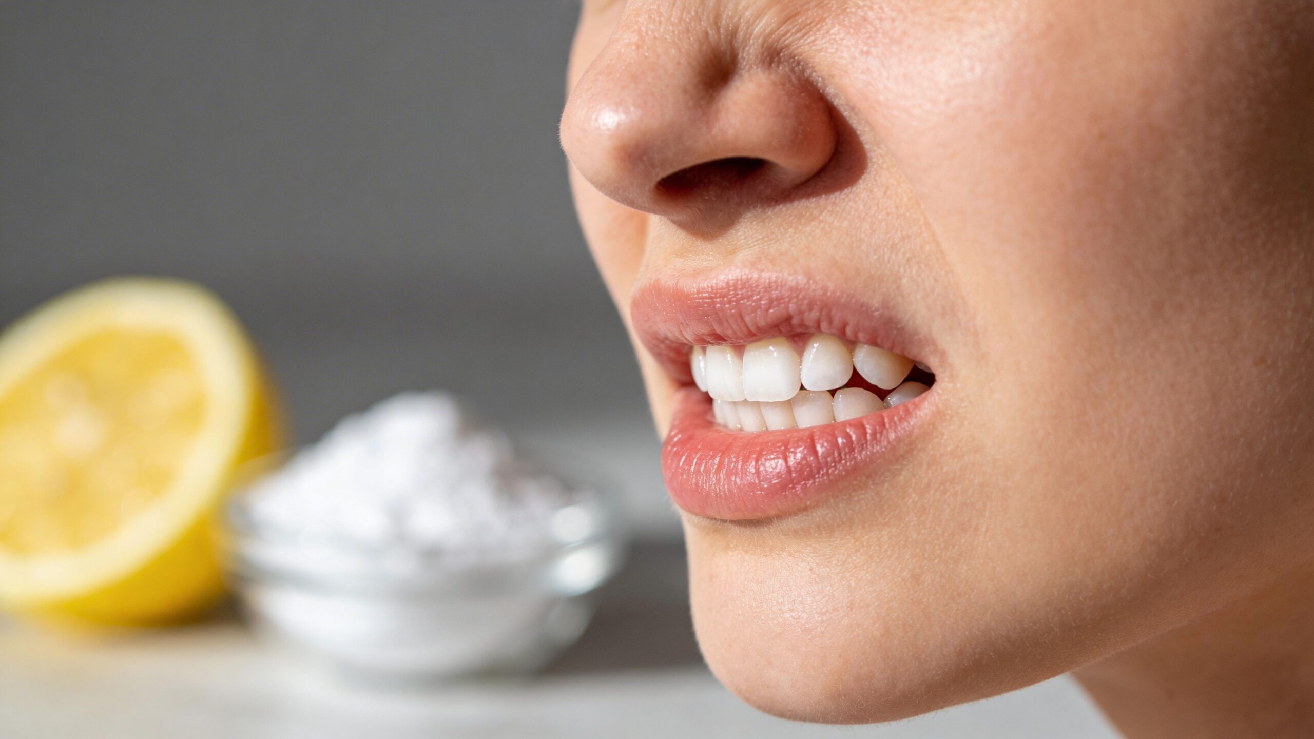 A close-up view of a woman clenching her teeth with a lemon and baking soda background.