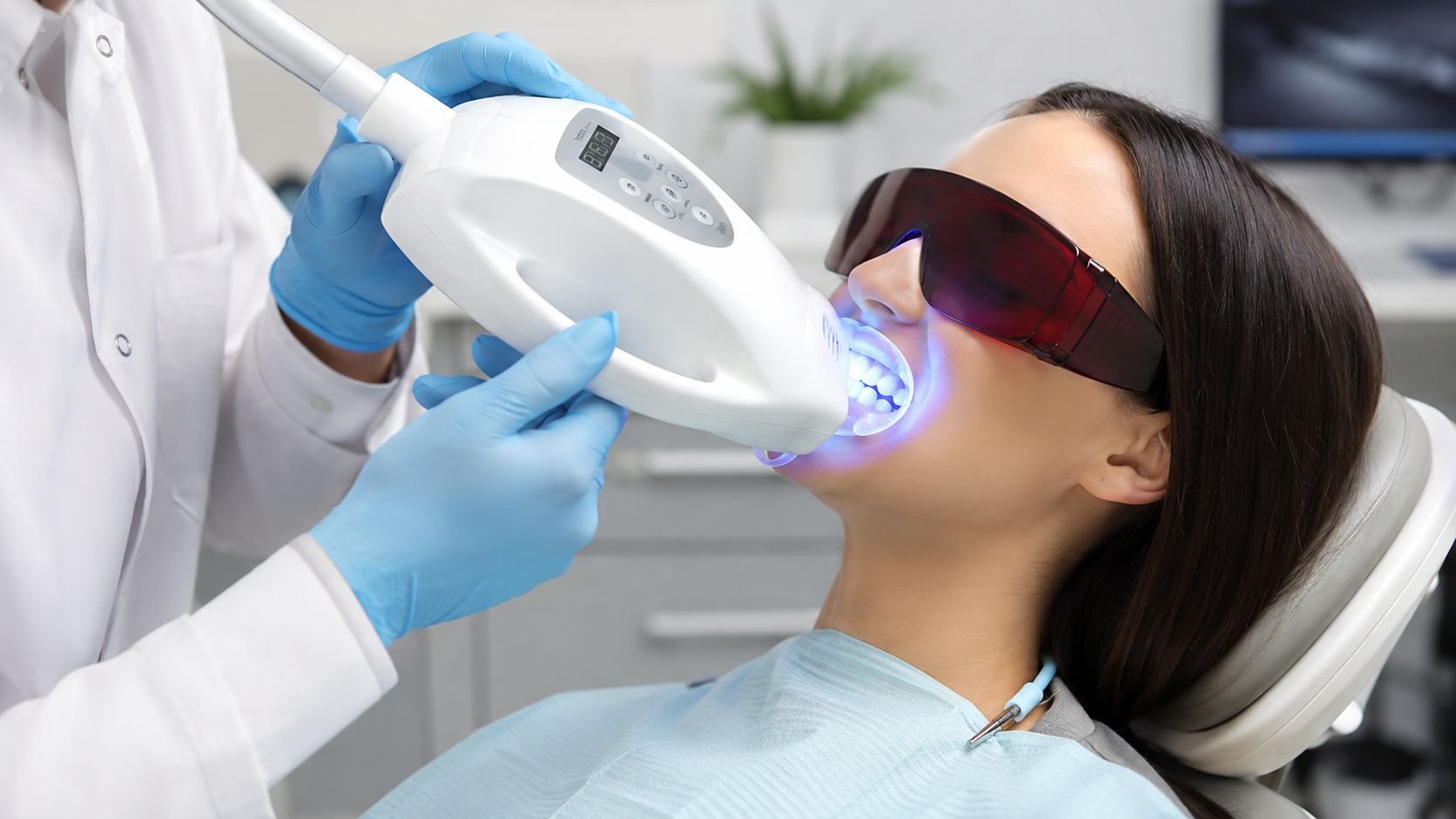 A professional dentist performing a laser teeth whitening treatment on a female patient in a dental clinic.