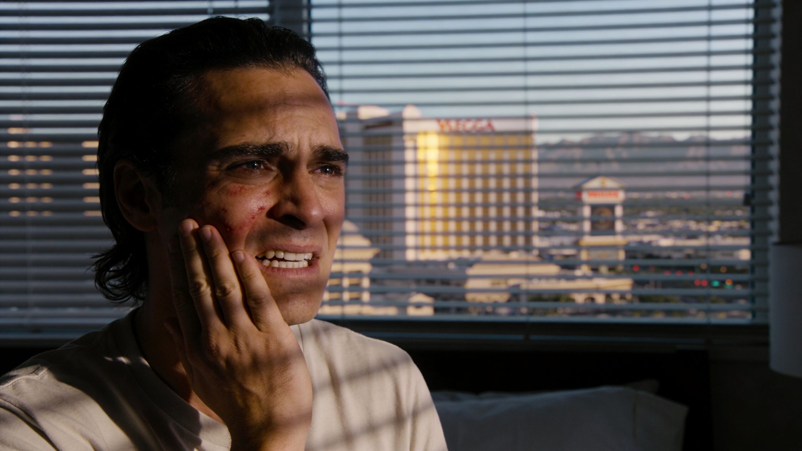 A man looking distressed while holding his face, possibly experiencing dental pain in a hotel room.