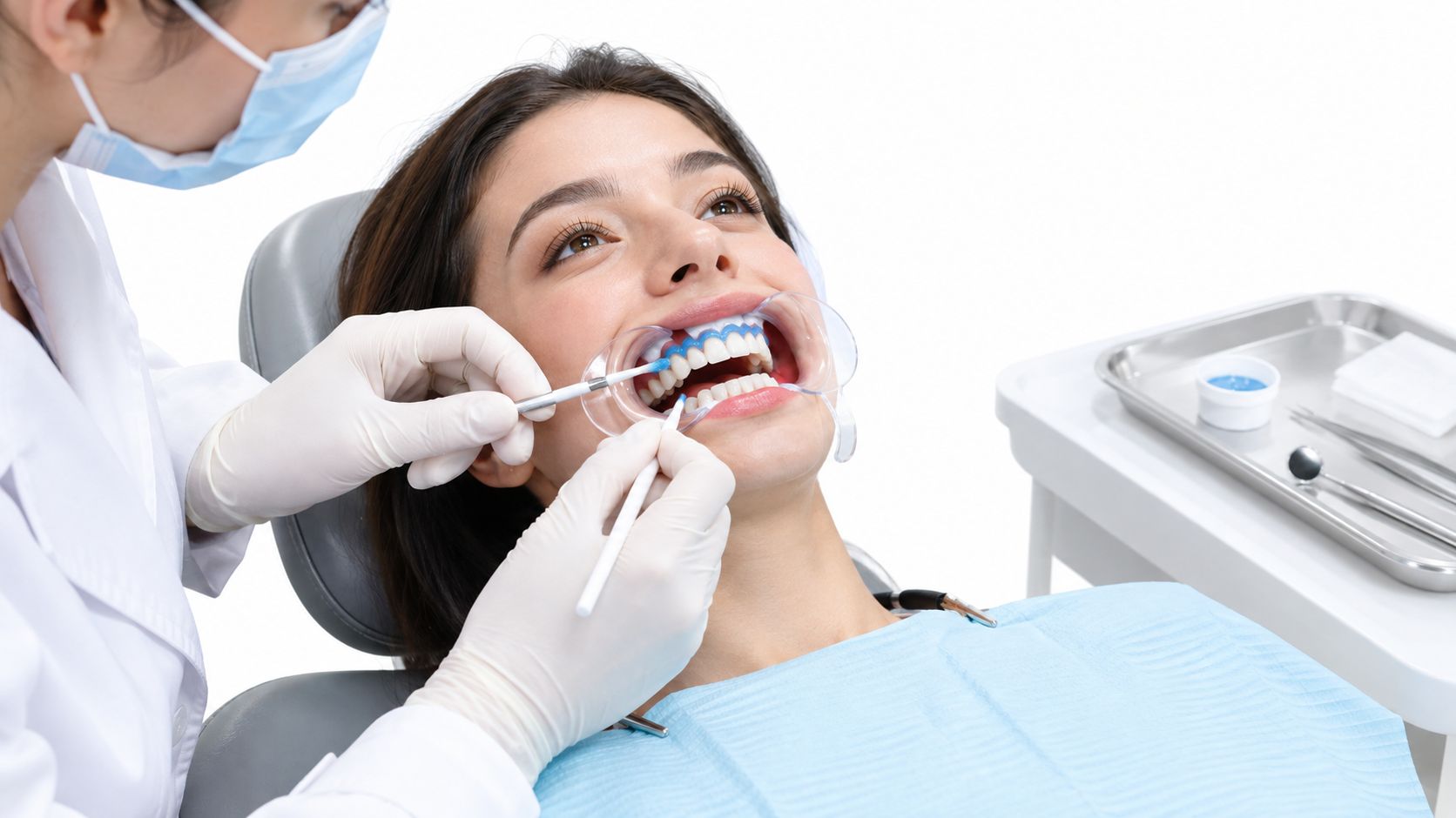 A professional dentist applying a whitening gel to a female patient's teeth during an office procedure.